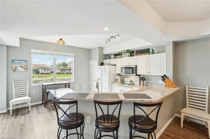 Kitchen featuring white appliances, white cabinetry, light hardwood / wood-style floors, a kitchen bar, and kitchen peninsula