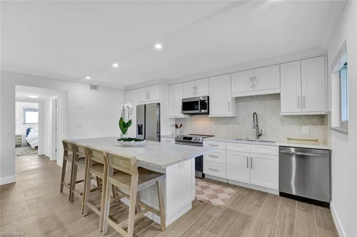 Kitchen with white cabinets, stainless steel appliances, wood finish floors, crown molding, and a breakfast bar