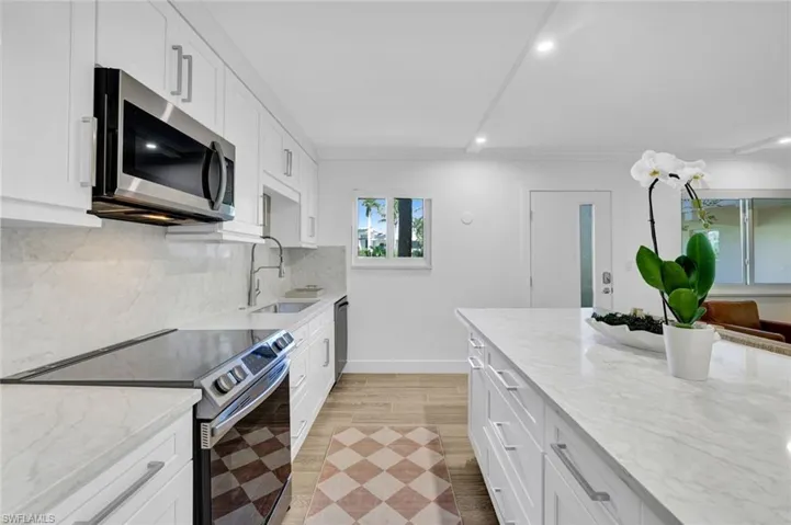 Kitchen with stainless steel appliances, white cabinetry, light stone counters, recessed lighting, and tasteful backsplash