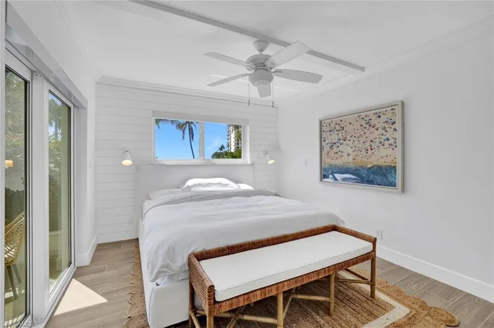 Bedroom featuring light wood finished floors, crown molding, access to exterior, wooden walls, and a ceiling fan