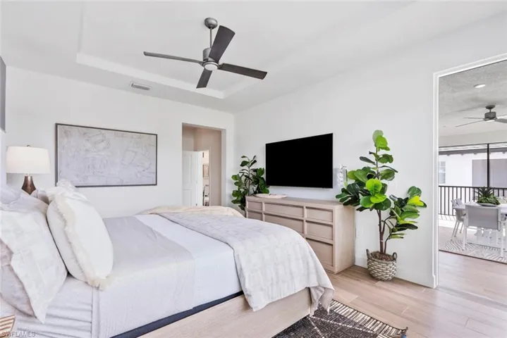 Bedroom with light hardwood / wood-style floors, ceiling fan, and a tray ceiling