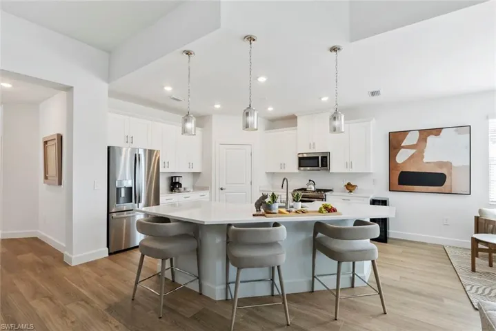Kitchen featuring hanging light fixtures, stainless steel appliances, light hardwood / wood-style flooring, an island with sink, and white cabinets