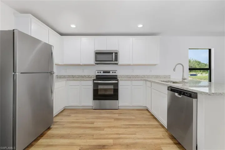 Kitchen with sink, stainless steel appliances, white cabinetry, and light wood-type flooring
