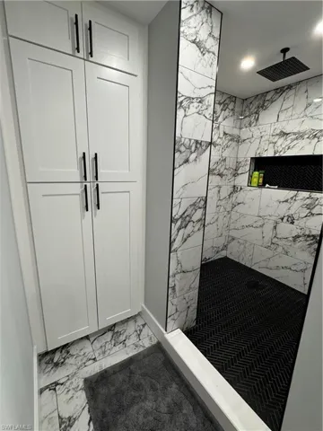 Full bathroom with baseboards, marble finish floor, and tiled shower