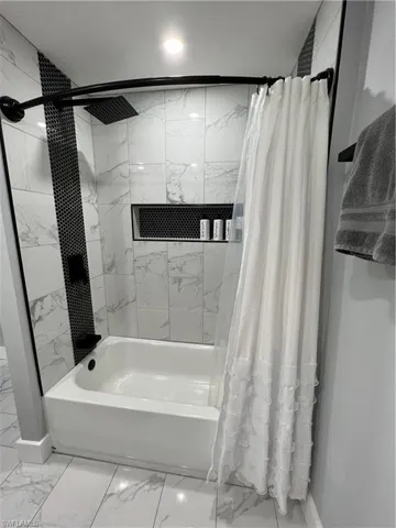 Bathroom with baseboards, marble finish floor, and shower / bath combination with curtain