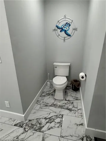 Bathroom featuring toilet, baseboards, and marble finish floor