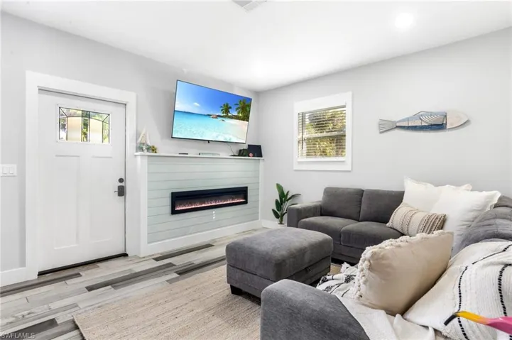 Living room with plenty of natural light, baseboards, a glass covered fireplace, and wood finished floors
