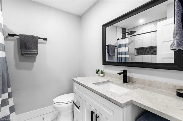 Bathroom featuring vanity, toilet, marble finish floor, baseboards, and curtained shower