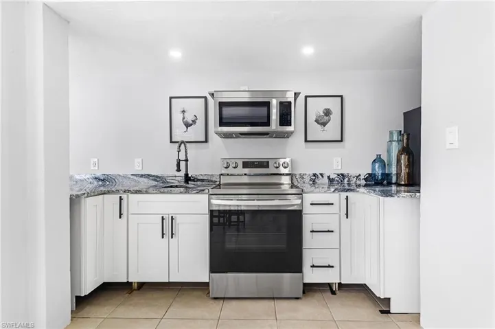 Kitchen featuring white cabinets, a sink, stone countertops, stainless steel appliances, and light tile patterned floors