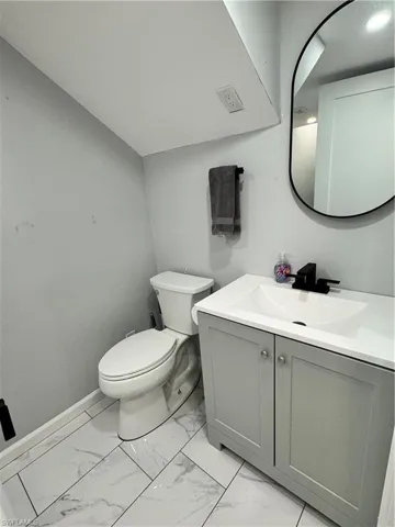Bathroom with toilet, baseboards, marble finish floor, and vanity