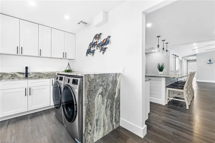 Clothes washing area with visible vents, a sink, baseboards, washer and dryer, and dark wood-type flooring