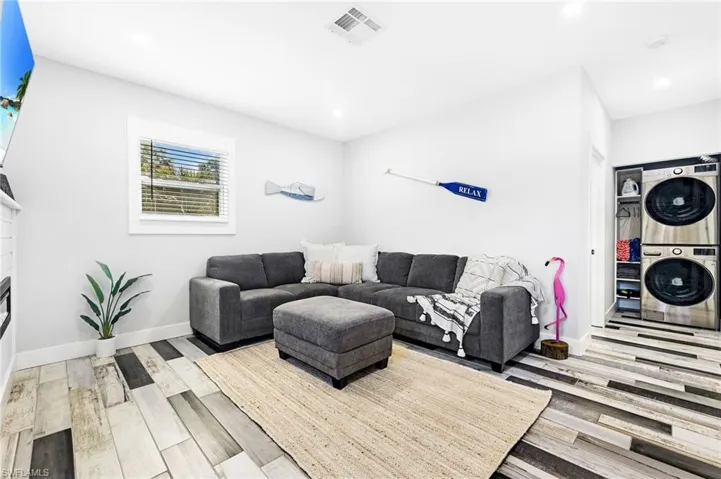 Living area featuring stacked washer and dryer, visible vents, wood finished floors, baseboards, and a glass covered fireplace