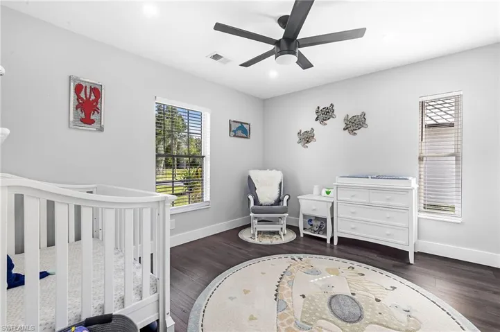 Bedroom with baseboards, visible vents, a crib, and wood finished floors