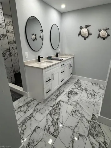 Full bath featuring a tile shower, a sink, double vanity, marble finish floor, and baseboards