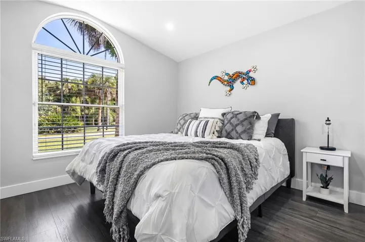 Bedroom with baseboards, multiple windows, dark wood-style floors, and lofted ceiling