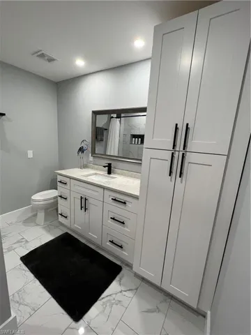 Full bath with baseboards, visible vents, marble finish floor, and vanity