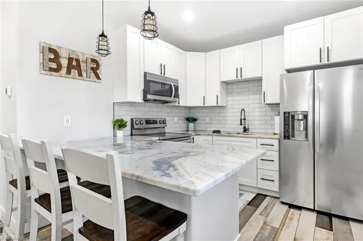 Kitchen featuring a peninsula, a breakfast bar, light stone counters, a sink, and stainless steel appliances
