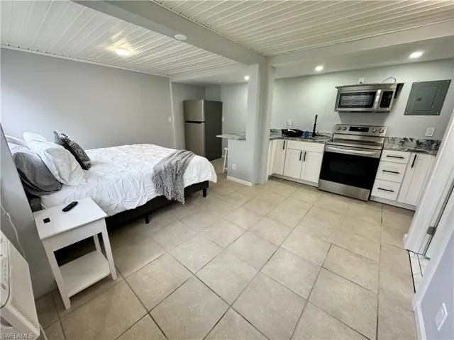 Bedroom with light tile patterned floors, freestanding refrigerator, recessed lighting, and electric panel