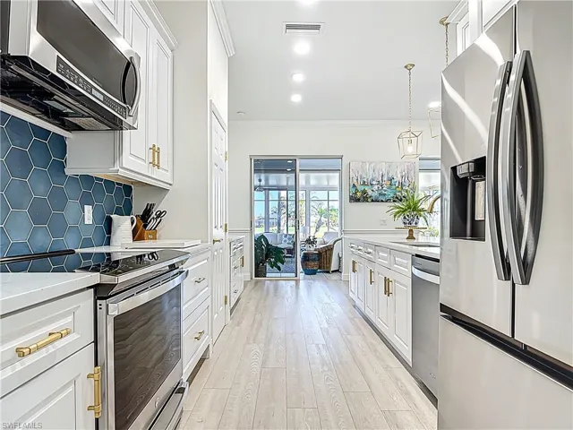 White shaker cabinetry with gold-tone hardware, stainless steel appliances, blue hexagonal tile backsplash, light wood-finish flooring, and recessed lighting