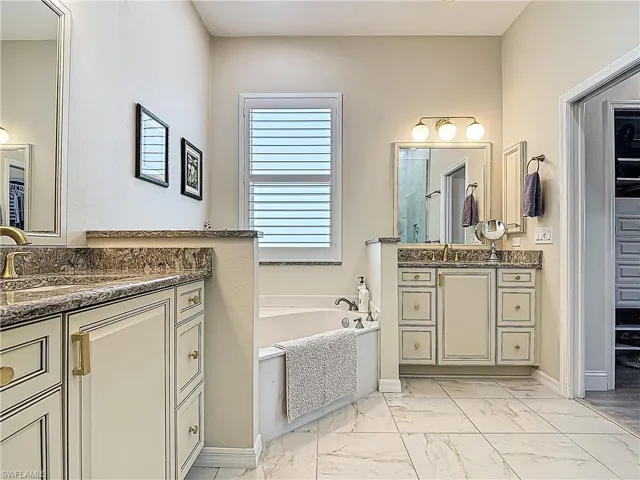 Dual vanities with stone countertops, an integrated soaking tub, tiled flooring, and a window with horizontal blinds