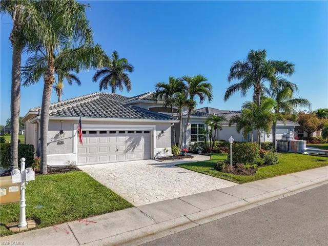 Stucco exterior with a tile roof, paver driveway, attached garage, and mature landscaping