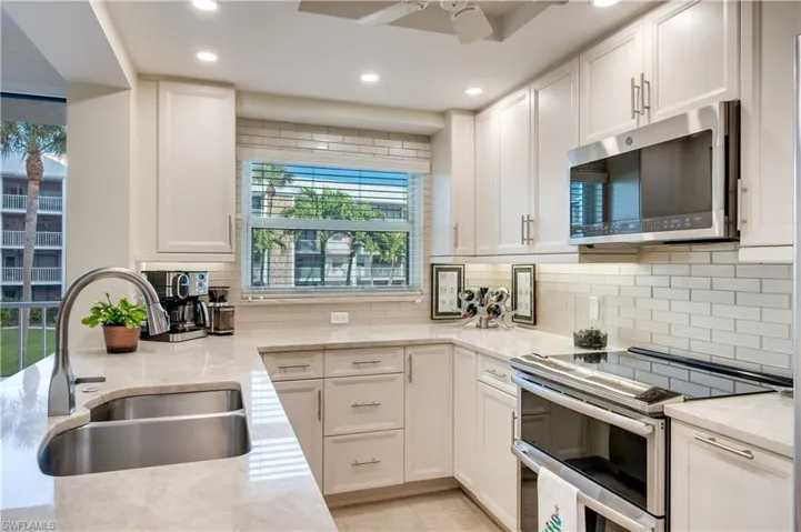 Kitchen with stainless steel appliances, light stone counters, white cabinetry, recessed lighting, and decorative backsplash
