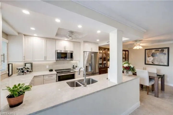 Kitchen with white cabinets, light stone counters, a peninsula, stainless steel appliances, and a ceiling fan