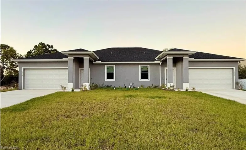 View of front of property with a garage, a lawn, stucco siding, and driveway