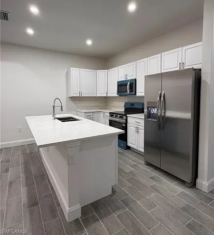 Kitchen with stainless steel appliances, wood tiled floors, white cabinetry, recessed lighting, and light stone countertops