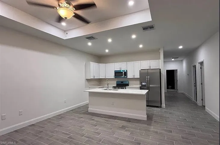 Kitchen featuring stainless steel appliances, white cabinetry, recessed lighting, a center island with sink, and wood finish floors