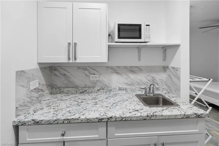 Kitchen featuring white microwave, white cabinetry, light stone counters, tasteful backsplash, and a ceiling fan
