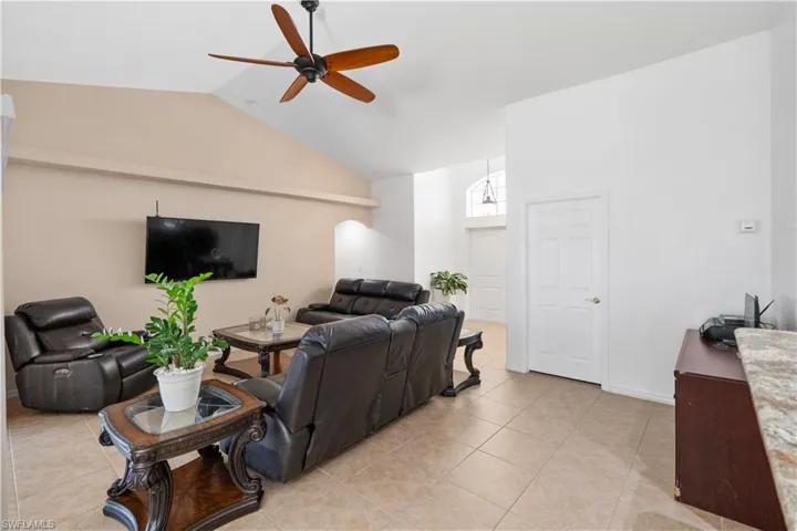 Living room featuring a ceiling fan, lofted ceiling, and light tile patterned floors