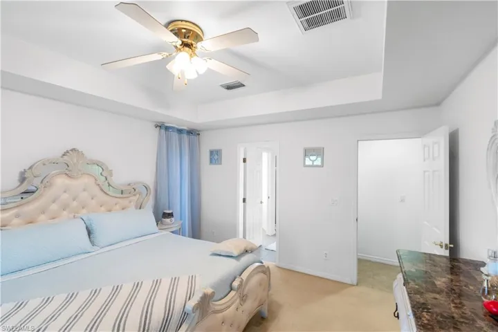 Bedroom featuring light colored carpet, a tray ceiling, and a ceiling fan