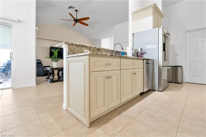 Kitchen with cream cabinetry, ceiling fan, light tile patterned floors, stainless steel appliances, and lofted ceiling