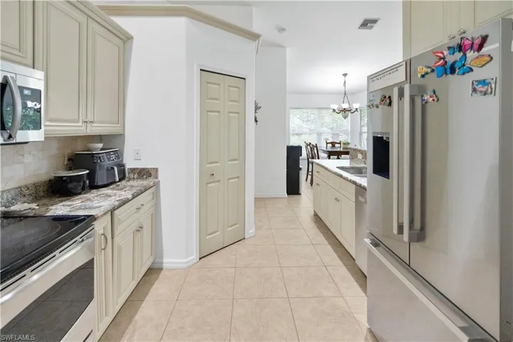 Kitchen with stainless steel appliances, light stone counters, cream cabinetry, light tile patterned floors, and decorative backsplash