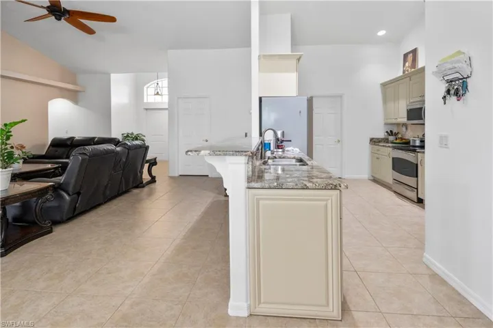 Kitchen featuring cream cabinets, open floor plan, a ceiling fan, light stone counters, and stainless steel appliances