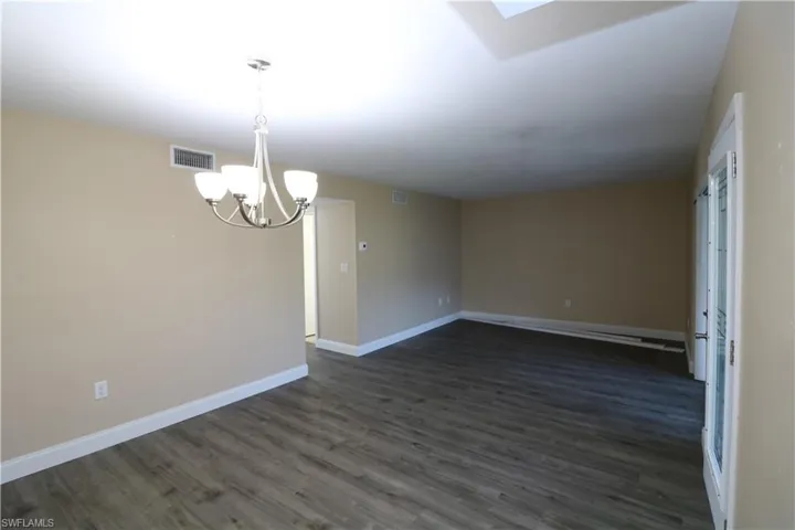 Unfurnished room featuring a chandelier, dark wood-style flooring, baseboards, and visible vents