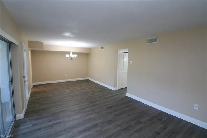 Empty room featuring a notable chandelier, baseboards, visible vents, and dark wood finished floors