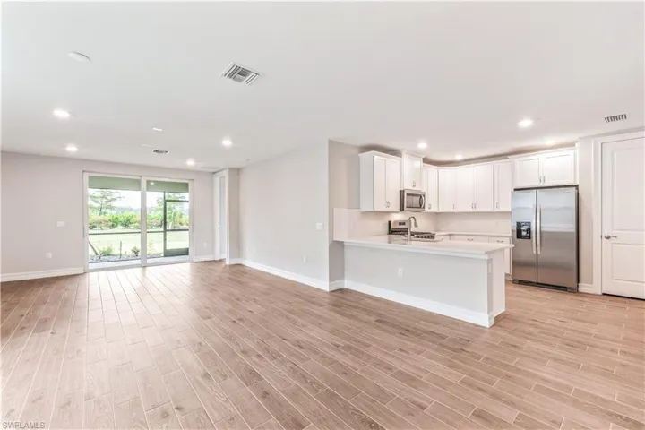 Kitchen with stainless steel appliances, white cabinetry, open floor plan, recessed lighting, and light wood-type flooring