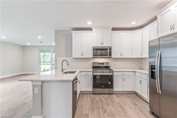 Kitchen with stainless steel appliances, wood finish floors, recessed lighting, white cabinetry, and a peninsula