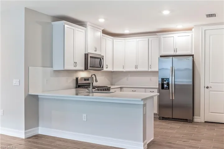 Kitchen featuring stainless steel appliances, wood tiled floors, white cabinetry, and recessed lighting