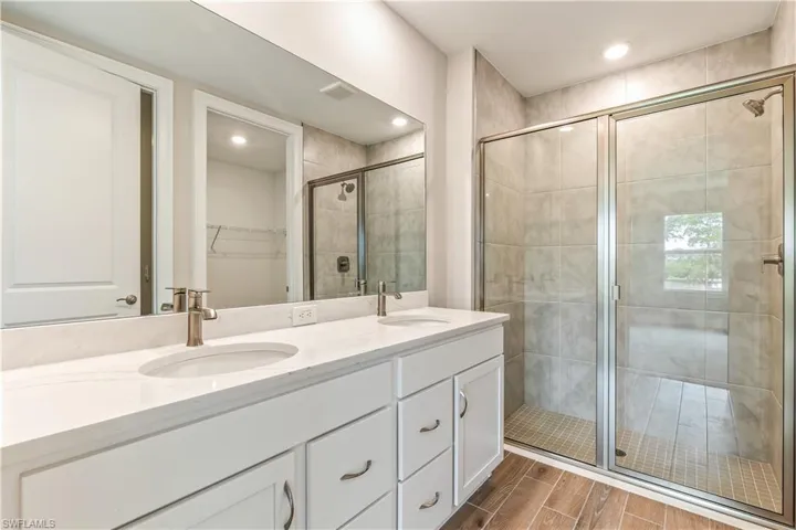 Full bath featuring a spacious closet, a shower stall, and wood finish floors