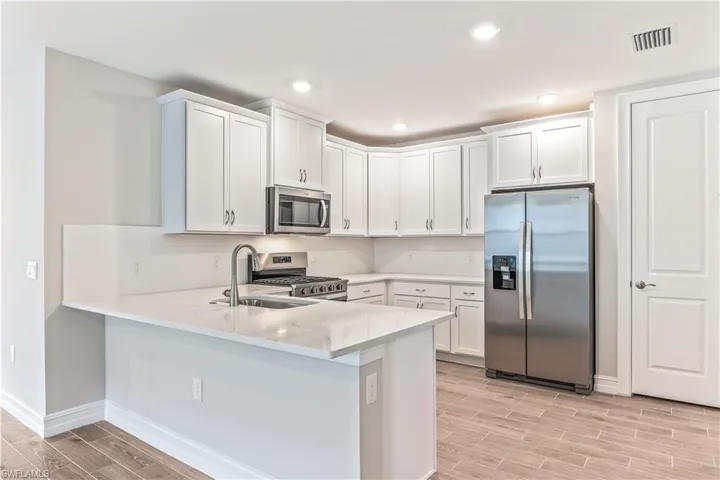 Kitchen featuring appliances with stainless steel finishes, wood tiled floors, white cabinetry, light stone counters, and recessed lighting