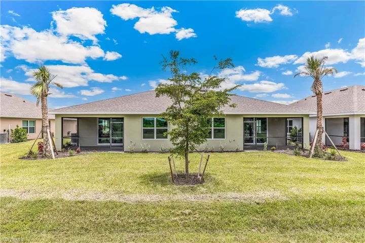 Back of property with stucco siding, a lawn, roof with shingles, and a sunroom