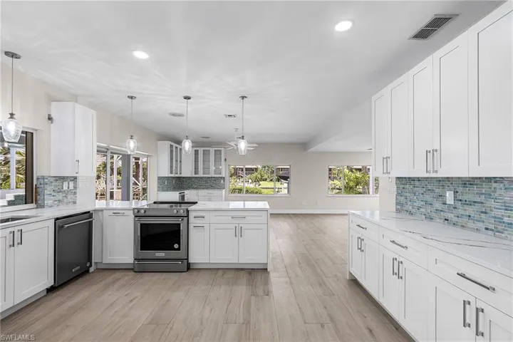 Kitchen featuring white cabinets, decorative backsplash, stainless steel appliances, and light stone counters