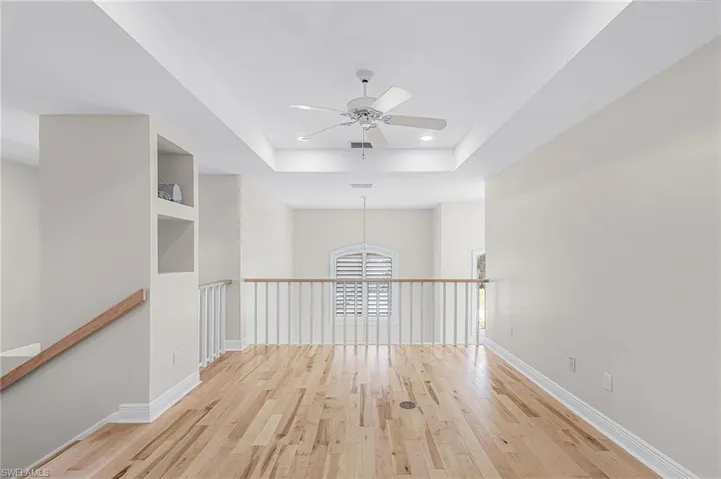 Loft featuring light wood-style flooring, a ceiling fan, a raised ceiling, and recessed lighting