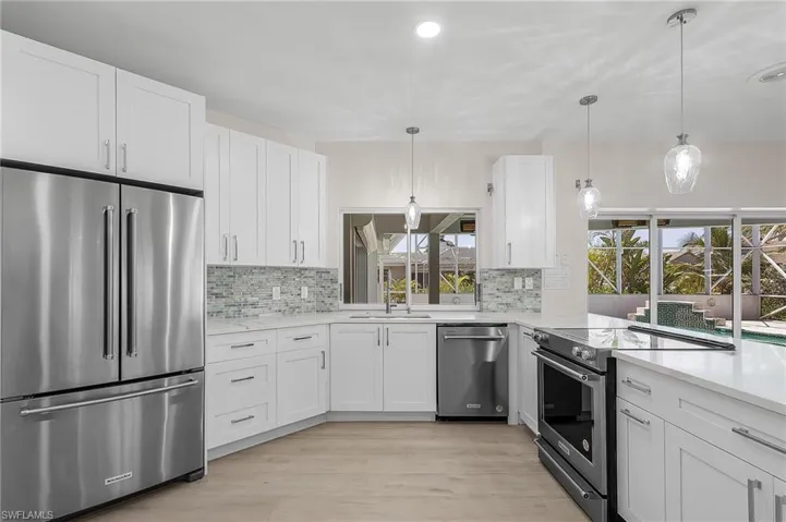 Kitchen featuring stainless steel appliances, white cabinetry, hanging light fixtures, light wood-style floors, and backsplash