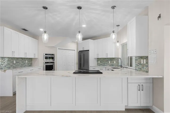 Kitchen featuring light stone countertops, pendant lighting, stainless steel appliances, and a peninsula