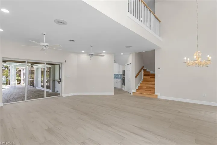Unfurnished living room featuring light wood-style floors, a chandelier, ceiling fan, and a high ceiling