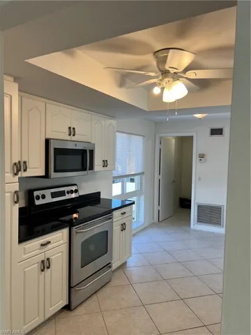 Kitchen featuring ceiling fan, light tile patterned floors, stainless steel range, and white cabinetry
